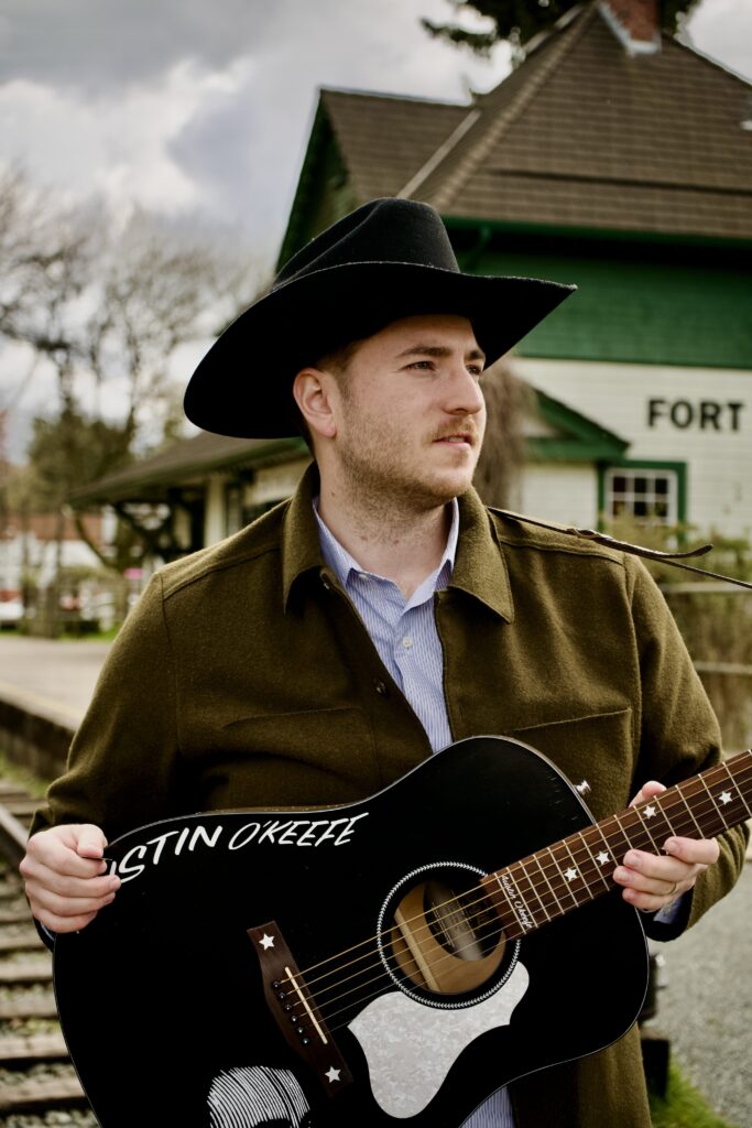 Austin T. O'Keefe, Canadian singer-songwriter, holding a custom black acoustic guitar with his name painted on the body.