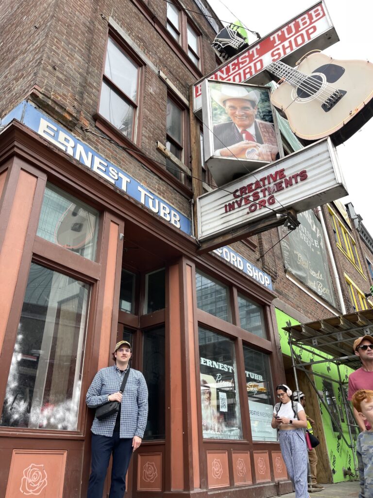Artist Austin T. O'Keefe standing in front of the historic Ernest Tubb Record Shop on Broadway in Nashville, featuring the iconic giant guitar sign and vintage brick storefront. The Sound of the Texas Troubadour: Bridging the Gap from Alberta to the 1970s. Ernest Tubb and Western Swing