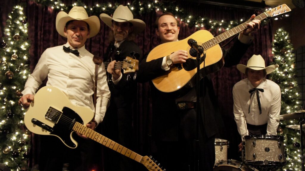 Austin T. O’Keefe and the Nostalgia Cowboys performing live in Alberta. Austin is singing and playing a Gibson acoustic guitar, flanked by bandmates with a Telecaster and bass, set against a backdrop of festive lights and Christmas trees. The Sound of the Texas Troubadour: Bridging the Gap from Alberta to the 1970s. Ernest Tubb and Western Swing