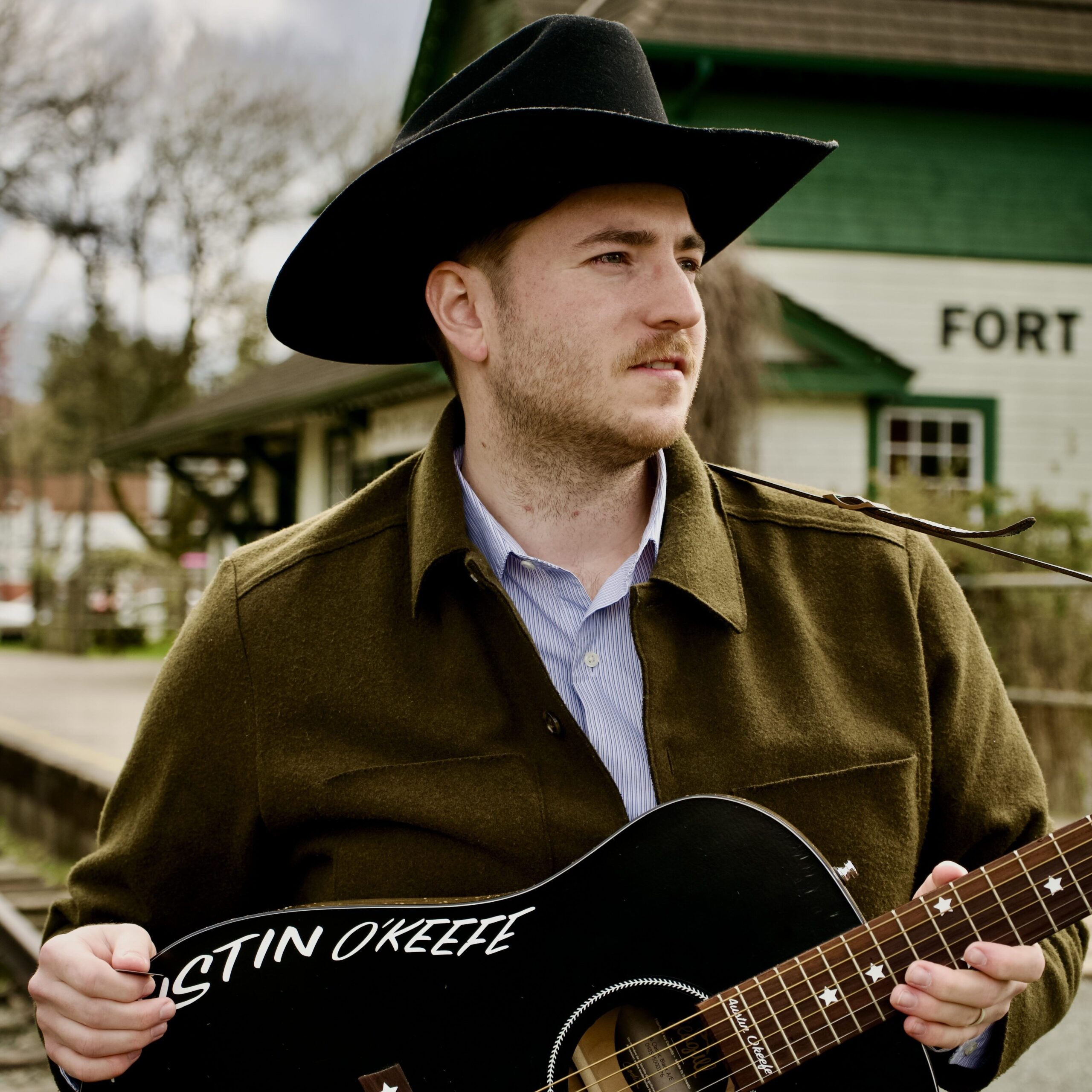 Austin T. O'Keefe, Canadian singer-songwriter, holding a custom black acoustic guitar with his name painted on the body.